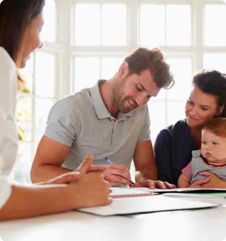 Man signing a document with his wife and child, while another woman watches over him.