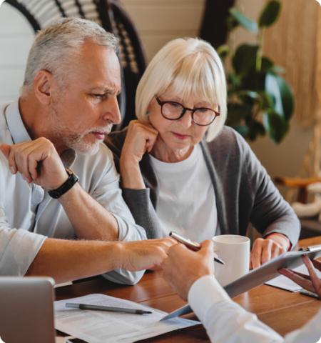 Older man and woman sitting at a table looking at tablet a woman is holding.