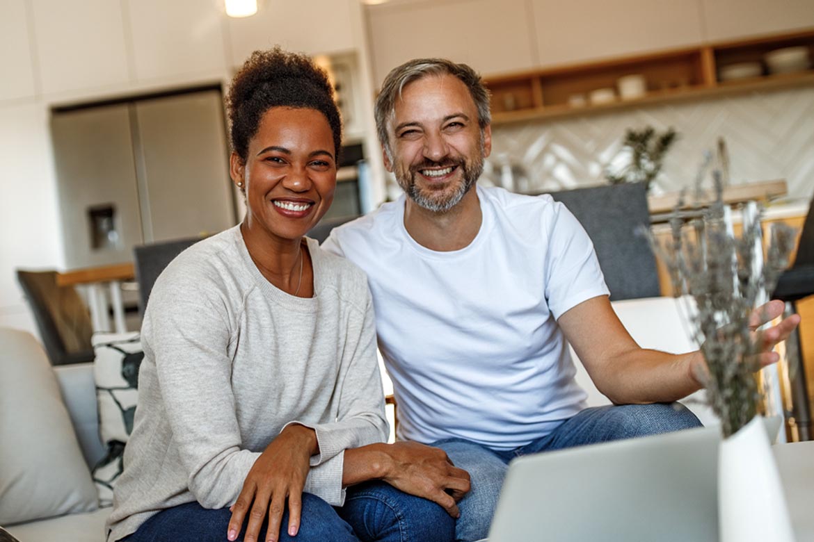 couple smiling in front of a computer looking into the camera